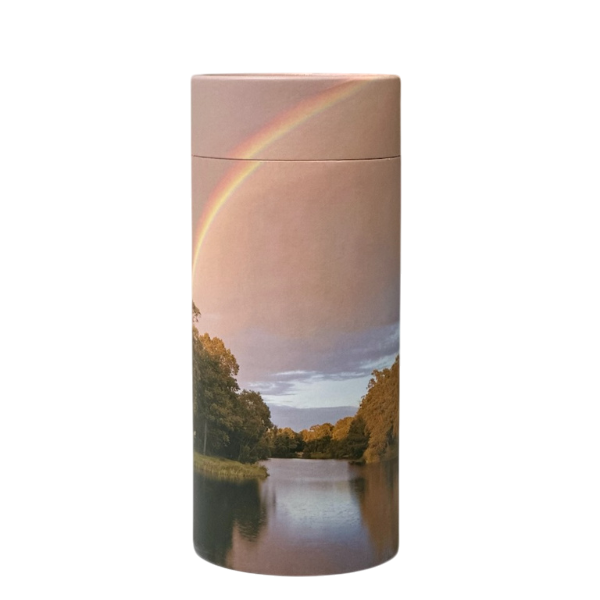 A cylindrical biodegradable urn featuring an image of a rainbow over a river, surrounded by trees under a partly cloudy sky—a beautiful choice for green burial in Australia. by H Parsons Funeral Directors