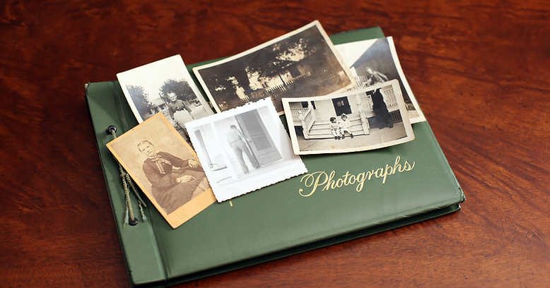 A green photo album labelled "Photographs" sits on a wooden surface with old black-and-white and sepia photos spread on top—perfect for gathering memorial ideas or inspiration for celebration of life ideas to honour loved ones. by H Parsons Funeral Directors
