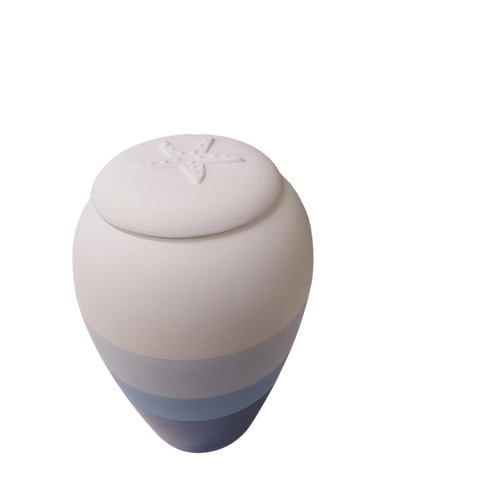 A ceramic biodegradable urn with a gradient design in shades of white and blue, featuring a rounded lid embossed with a starfish, ideal for green burial, set against a plain white background. by H Parsons Funeral Directors