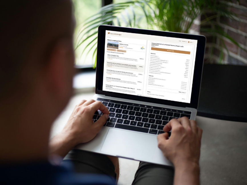 A person is using a laptop, viewing financial or investment documents on the screen. The background is blurred, with a green plant and window visible—perhaps researching funeral trends Australia or exploring eco-friendly burials. by H Parsons Funeral Directors