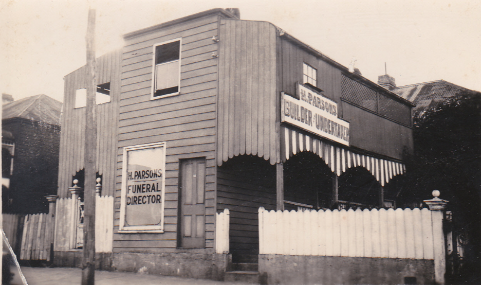 A vintage black-and-white photo of the H. Parsons Funeral Director building, marking over 130 years of local funeral service. Signs read "H. Parsons Funeral Director" and "Undertaker," with a picket fence and an awning with scalloped edges. by H Parsons Funeral Directors