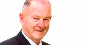 An older man with short, thinning grey hair wearing a dark suit and white shirt is smiling slightly against a plain white background. by H Parsons Funeral Directors