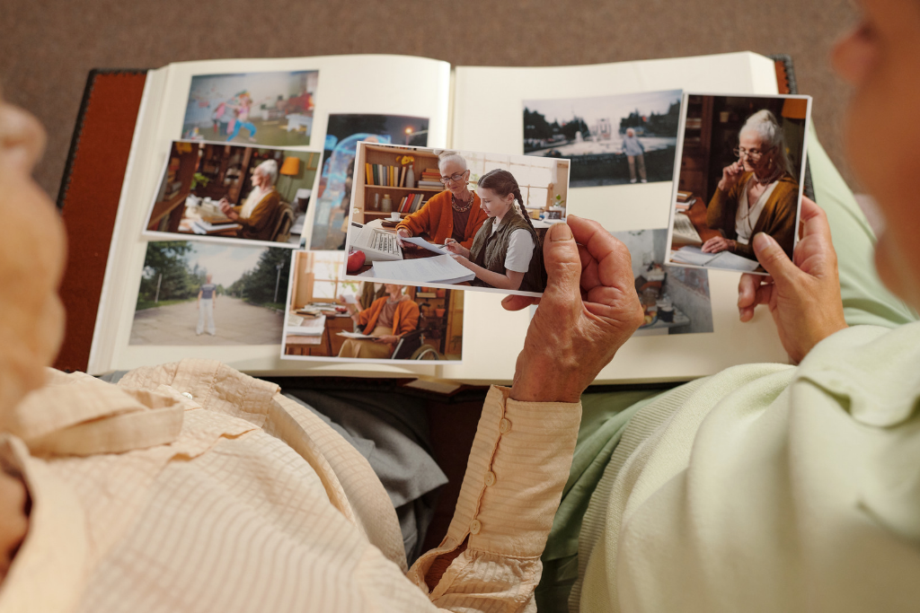 Two people look through an open photo album, sharing in their understanding of grief as they hold a picture of an older woman and review papers together. by H Parsons Funeral Directors